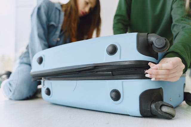 Young women closing luggage bag on floor